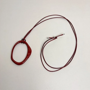 Detail view of a long adjustable leather cord necklace with irregular red ceramic pendant