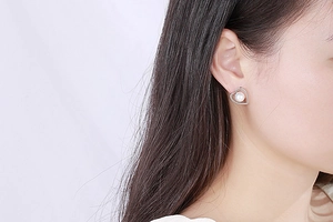 Close-up of heart-shaped silver earrings with white pearl detail on female model