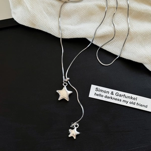 Detail of silver asymmetric double star necklace with snake chain on black background