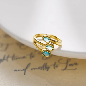 Detail of gold three-layer ring with three oval blue zircons on vintage paper background