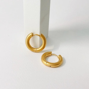 Macro view of thick matte gold hoops with minimalist brushed finish and hidden clasps