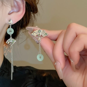 Detail of silver fan-shaped earrings with green stones and long metal tassel fringe