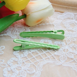 Detailed view of wave-shaped green metal hair clips on white lace with tulips