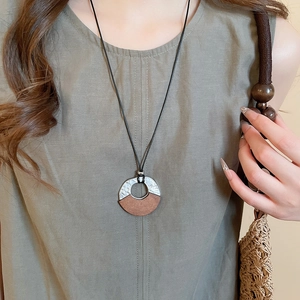 Detail of round wood and metal geometric pendant on black cord minimalist necklace