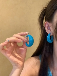 Close-up of a blue acrylic geometric C-shaped hoop earring worn by a model