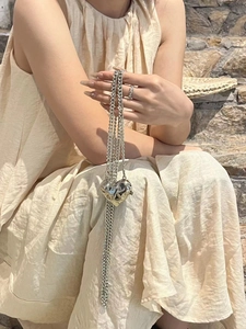 Detail of a silver heart-shaped pendant with long metal chain held in a natural setting