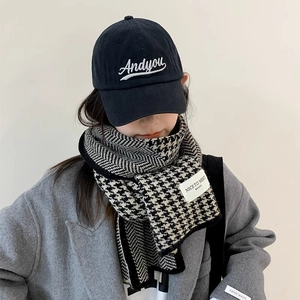 Knitted houndstooth scarf paired with black embroidered baseball cap and wool coat