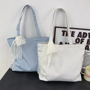 Detail of canvas tote bag with polka dot straps and lace bow charm on dark surface
