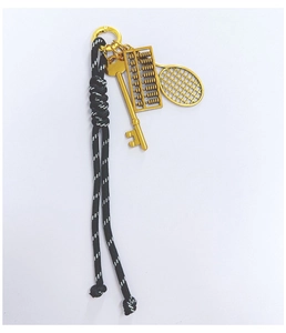 Detailed view of woven black and white cord keychain with golden abacus and racket charms