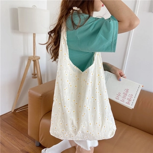 Detailed view of white canvas tote bag with yellow daisy print worn by model