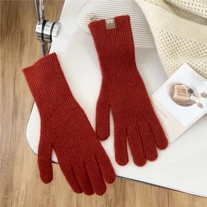 Detail of terracotta knitted gloves with ribbed texture and woven brand logo tag