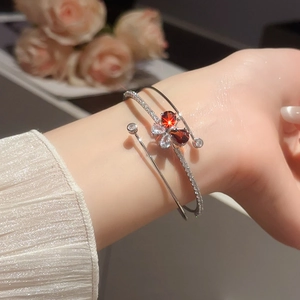 Dettaglio del bracciale a tre strati in argento con cuore rosso e farfalla di zirconi