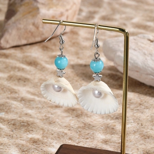 Detail of ocean-style shell earrings with blue beads and pearls on beach background