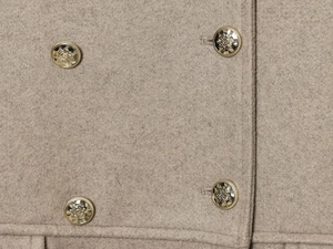 Detailed view of beige wool blend coat texture and ornate golden embossed buttons