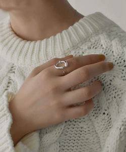 Close-up of a silver minimalist open ring on a finger with a white knitted sweater background
