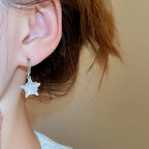 Close-up of sparkling star-shaped zircon pendant earring on model ear for women