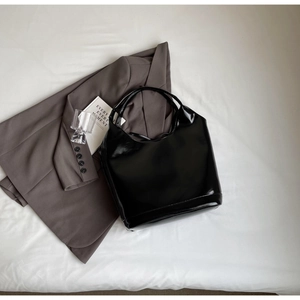 Minimalist black patent leather shoulder bag styled with a grey blazer and accessories