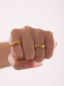 Detail of two wavy gold minimalist rings worn on hand against a white background
