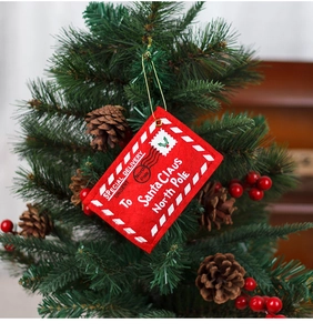 Detail of red felt Christmas envelope ornament hanging on tree branch with pine cones