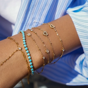 Detail of 18k gold stainless steel layered bracelet with turquoise beads and heart charms