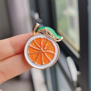 Macro shot of an orange slice enamel brooch with golden metal edges held by fingers