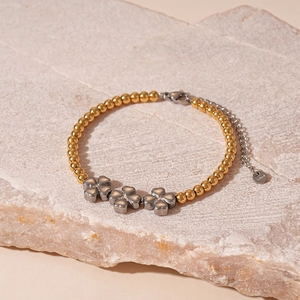 Détail des trèfles sur un bracelet en acier inoxydable doré avec arrière-plan en pierre