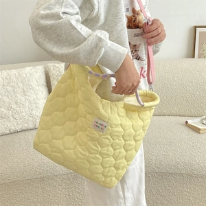 Gros plan du sac matelassé jaune avec bandoulière rose et poignée violette sur canapé