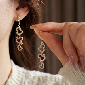 Detail of gold-plated dangling earrings featuring red heart charms and white zircon stones
