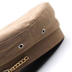 Detail of brown baker boy hat featuring ribbed fabric texture and gold chain decoration