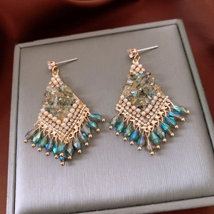 Detail of bohemian gold tassel earrings with teal crystals and faux pearls on satin