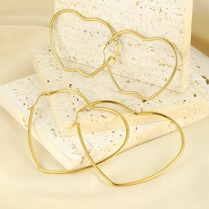 Detail of gold-plated heart and apple shaped hoop earrings on a beige stone stand