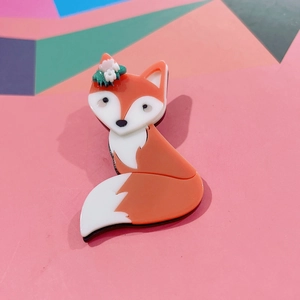 Cute orange acrylic fox brooch with small flower details on a soft pink background