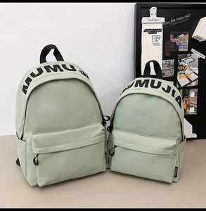 Close-up of green nylon backpacks in two sizes with MUMUJIA logo and side pockets