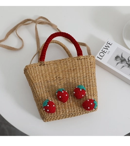Détail du sac en paille fait main avec fraises au crochet et poignée en velours rouge