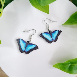 Macro detail of elegant blue butterfly wing earrings with metal hooks on a white tray