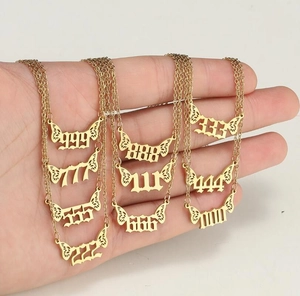 Détail de colliers multicouches en acier plaqué or 18 carats avec pendentifs chiffres anges