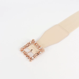 Close-up of beige elastic belt featuring a gold square buckle with rhinestone leaf patterns