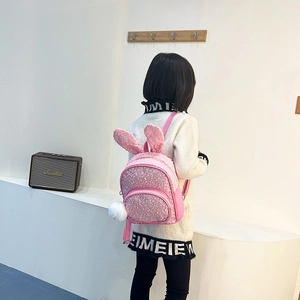 Pink sequin kids backpack with 3D bunny ears and white pom-pom charm on model