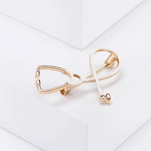 Detailed close-up of a gold stethoscope brooch with white enamel finish on a white background