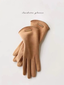 Close-up of brown suede gloves with soft fleece lining and golden metal logo plate