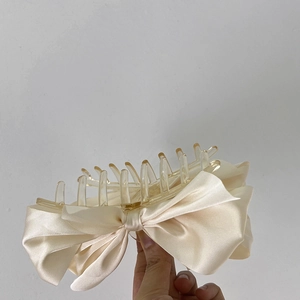 Macro detail of large cream satin bow hair claw clip showing elegant fabric texture