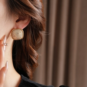 Close-up of a model wearing a gold square stud earring set with sparkling zircons