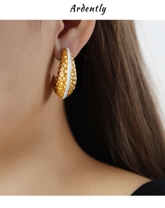 Macro shot of gold-plated cashew earrings featuring white enamel and hammered texture