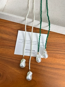 Detailed view of long pearl and green spinel necklaces on rustic wood background