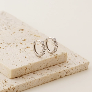 Detailed view of silver star huggie earrings with zircon inlays on stone props