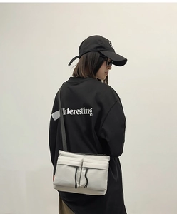 Close-up of white nylon messenger bag with double front pockets and black drawstrings