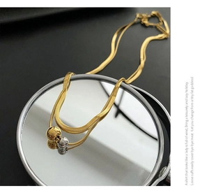 Macro detail of a double-layered gold snake chain necklace with three polished metal beads