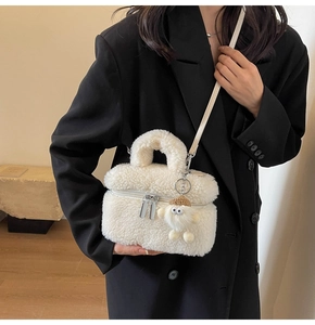 Detailed view of white faux shearling handbag with silver zippers and plush sheep charm