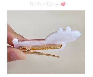 Detail of a pink and white acrylic Christmas cat hair clip with a golden metal fastener