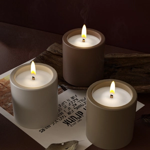 Three lit minimalist cylindrical aroma candles in matte finish on rustic wooden blocks